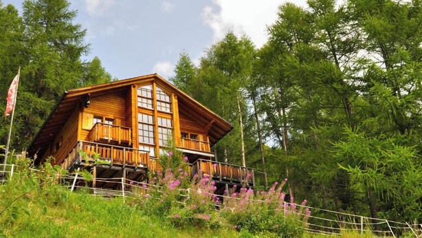 A wooden cabin with a balcony, surrounded by lush greenery and trees. - Très beau chalet contemporain avec une vue splendide !Très lumineux, construction sur 3 niveaux, sit (St-Luc)