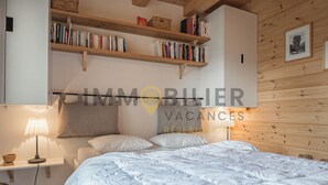 A bedroom with a bed, shelves with books, a lamp, and a wooden headboard. - Très beau chalet contemporain avec une vue splendide !Très lumineux, construction sur 3 niveaux, sit (St-Luc)
