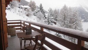 A wooden balcony with a table and chairs, overlooking a snowy mountain landscape. - Très beau chalet chaleureux et confortable, meublé et décoré avec beaucoup de goût. Spacieux et lumi (St-Luc)