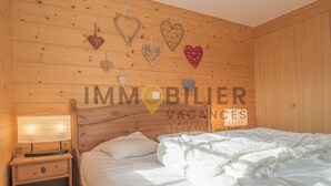 A wooden-paneled room with a bed, a nightstand, and decorative heart-shaped wall hangings. - Très beau chalet chaleureux et confortable, meublé et décoré avec beaucoup de goût. Spacieux et lumi (St-Luc)