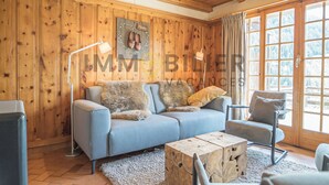 A cozy living room with a blue sofa, a wooden coffee table, and a chair. A wooden wall with a shoe rack and a lamp is visible. - Ideally located near the old village and a 2-minute walk from the funicular railway. Two-storey chal (St-Luc)