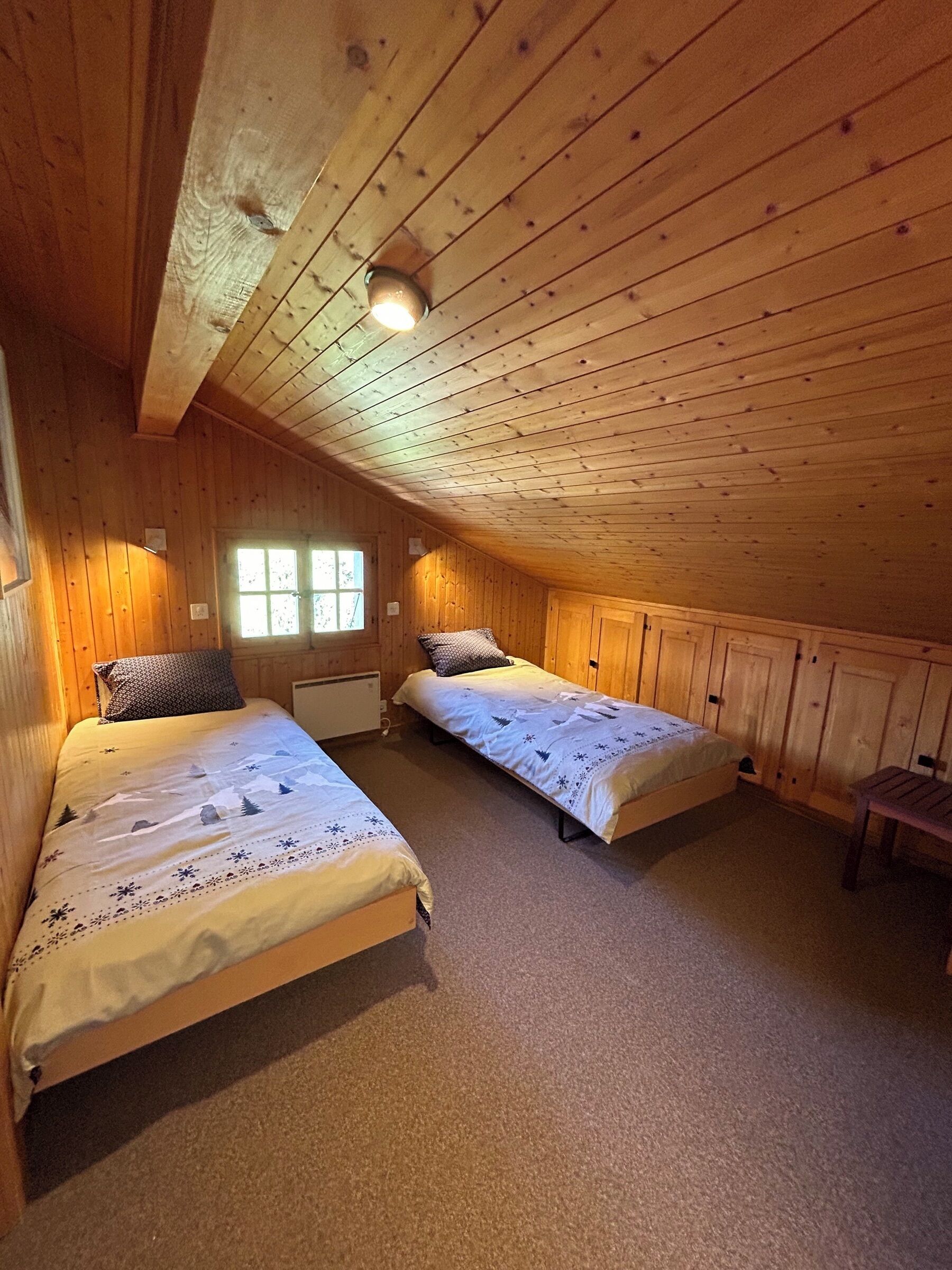 A cozy attic bedroom with two single beds, wooden walls, and a sloped ceiling.