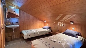A cozy cabin-style room with two single beds, a wooden ceiling, and a small bathroom with a sink and mirror. - Idéalement situé, au pied des pistes, en face du funiculaire. Appartement agréable et chaleureux, au (St-Luc)