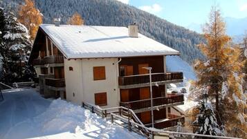 Un bâtiment de style chalet, doté d’un toit en pente, de balcons en bois et surplombant un paysage enneigé.