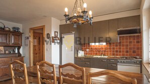 A kitchen with wooden cabinets, a stove, and a dining table with chairs. - Au pied des pistes, en face du funiculaire et à 5' à pied du centre du vieux village ! Appartement c (St-Luc)