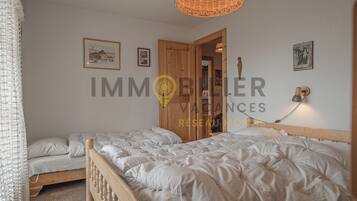 Une chambre avec deux lits, une armoire en bois et un luminaire suspendu.