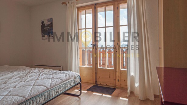 A bedroom with a bed, a wooden door, and a view of a balcony. - Idéalement situé, au pied des pistes, en face du funiculaire et à 5' à pied du centre du vieux villa (St-Luc)