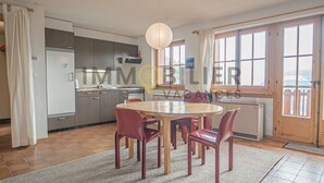 A modern kitchen with a dining area, featuring a round table and chairs, a hanging light fixture, and large windows with curtains. - Idéalement situé, au pied des pistes, en face du funiculaire et à 5' à pied du centre du vieux villa (St-Luc)