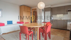 A modern kitchen with wooden cabinets, a dining table with red chairs, and a white ceiling light. - Idéalement situé, au pied des pistes, en face du funiculaire et à 5' à pied du centre du vieux villa (St-Luc)