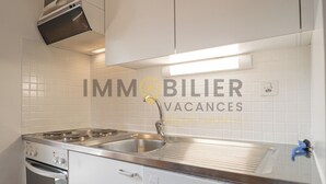 A modern kitchen with stainless steel appliances, a double sink, and white tiled walls. - Idéalement situé, au pied des pistes, face au funiculaire et à 5 minutes à pied du centre du vieux v (St-Luc)