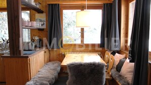 A cozy cabin interior with a wooden dining table, benches, and a large window with curtains. - Charmant 2 pièces pour 2 à 4 personnes au rez d'un chalet. Situé à 300 mètres de l'arrêt du bus nave (Chandolin)