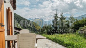 Un patio de piedra con mesa y sillas, una puerta de madera y vistas a montañas y vegetación.