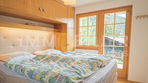 Un dormitorio con cama, armarios de madera y un ventanal con vistas al verdor.