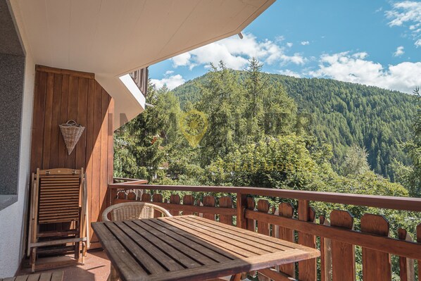 A wooden deck with a table and chairs, overlooking a forested mountain.