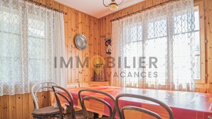 A dining area with a wooden interior, a table with a red tablecloth, and four metal chairs. - Appartement pour 5 personnes au rez-de-chaussée situé à seulement 300 mètres des pistes et bénéficia (St-Luc)