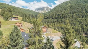 A mountainous area with wooden buildings, a winding road, and a clear sky. - Appartement pour 5 personnes au rez-de-chaussée situé à seulement 300 mètres des pistes et bénéficia (St-Luc)