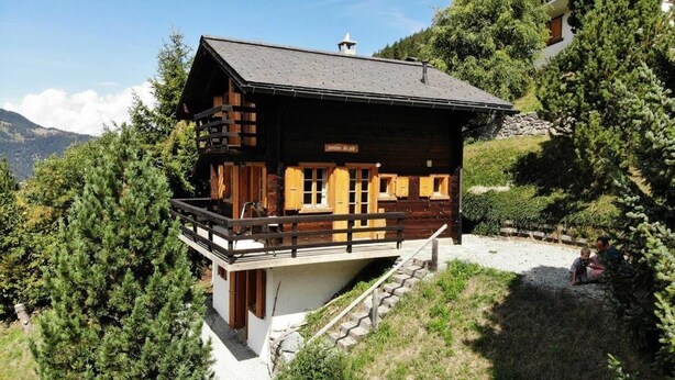 A wooden chalet with a balcony, surrounded by trees and mountains.