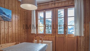 A wooden interior with a dining table, chairs, a small refrigerator, and a window with a mountain view.
