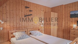 A wooden-paneled room with two beds, a nightstand, a dresser, and a wall-mounted lamp.