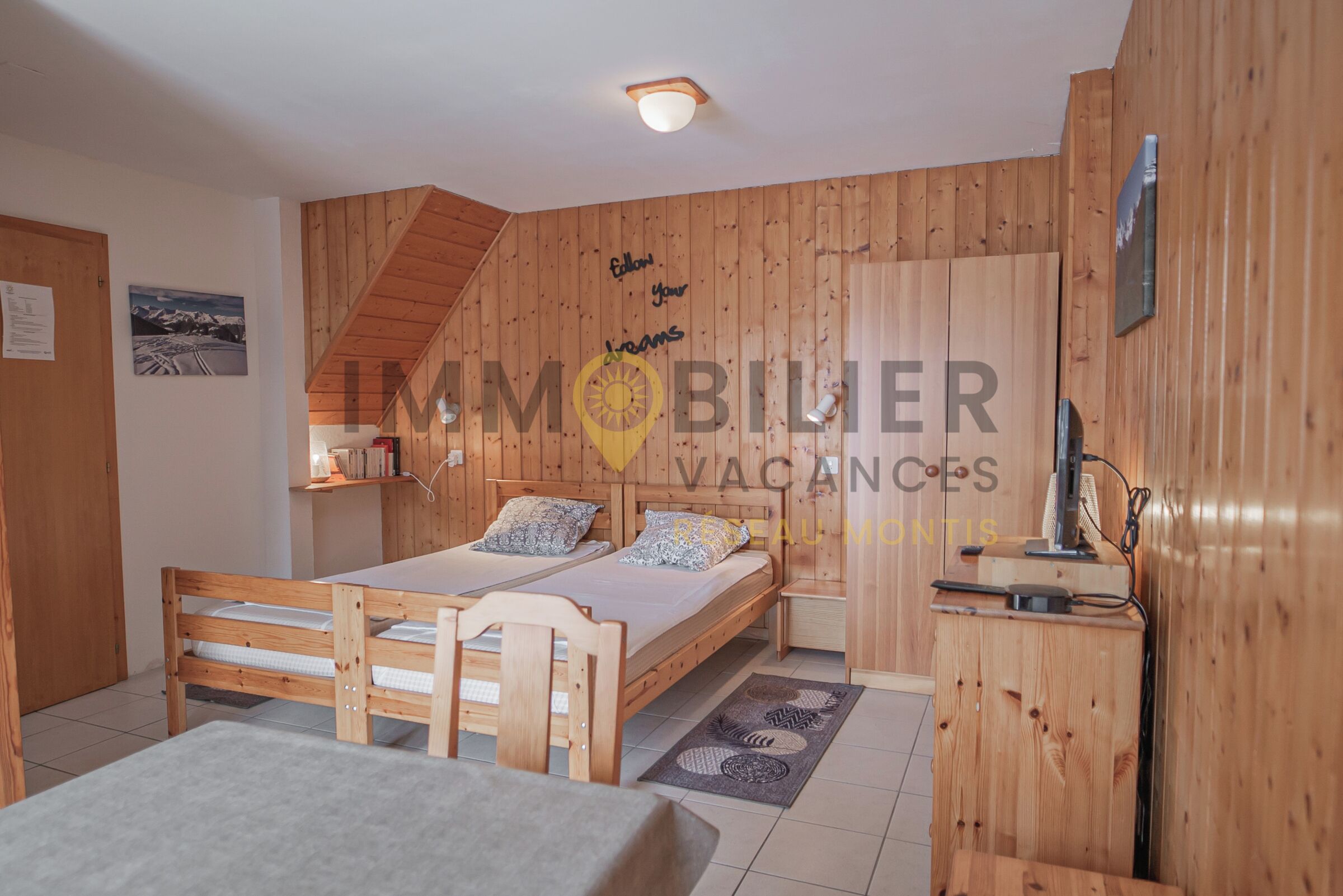 A wooden cabin-style bedroom with two beds, a desk, and a wardrobe.