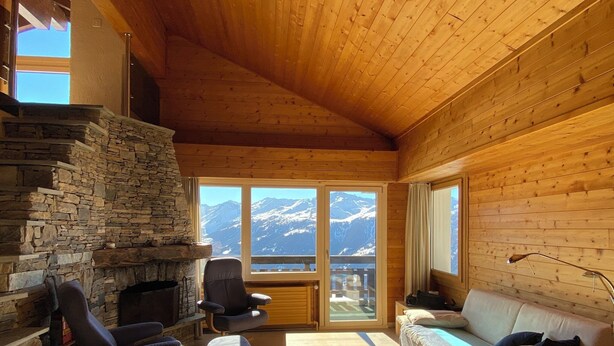 A cozy room with a stone fireplace, wooden ceiling, and a sofa. - Duplex de 3,5 pièces (75 m2) pour 4-5 personnes très lumineux, situé en face de l’Office du tourisme (Chandolin)