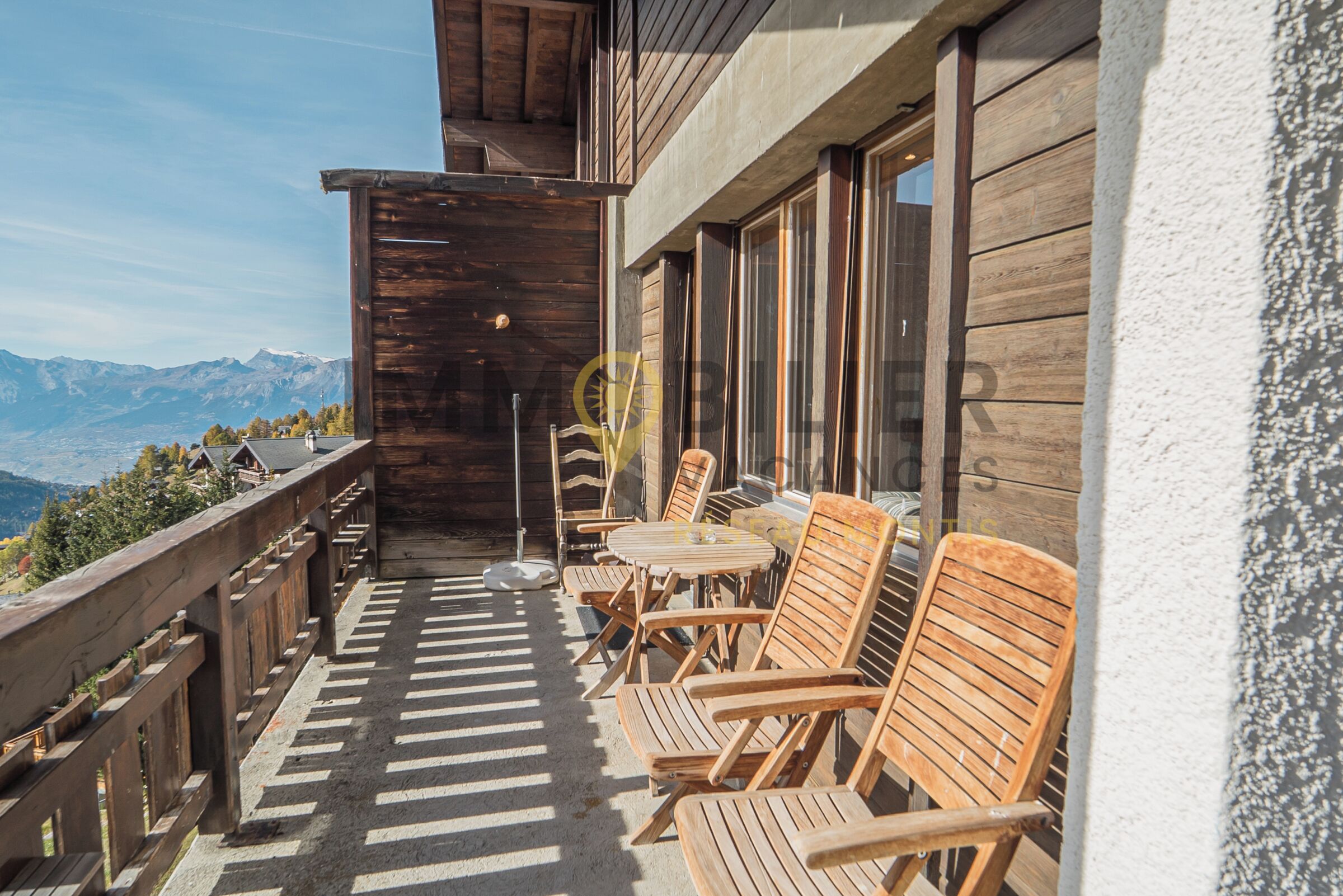 Un balcón de madera con mobiliario exterior y vistas a montañas.