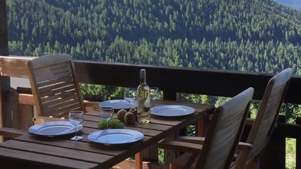 A wooden table set for two with plates, glasses, and a bottle, overlooking a forested mountain range. - Situé au centre de Chandolin dans une petite résidence, proche de toutes commodités et du bus navett (Chandolin)