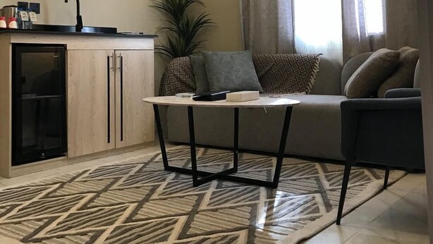 Een moderne woonkamer met een bank, een salontafel, een aan de muur bevestigde televisie en een keuken met een spoelbak en kasten.