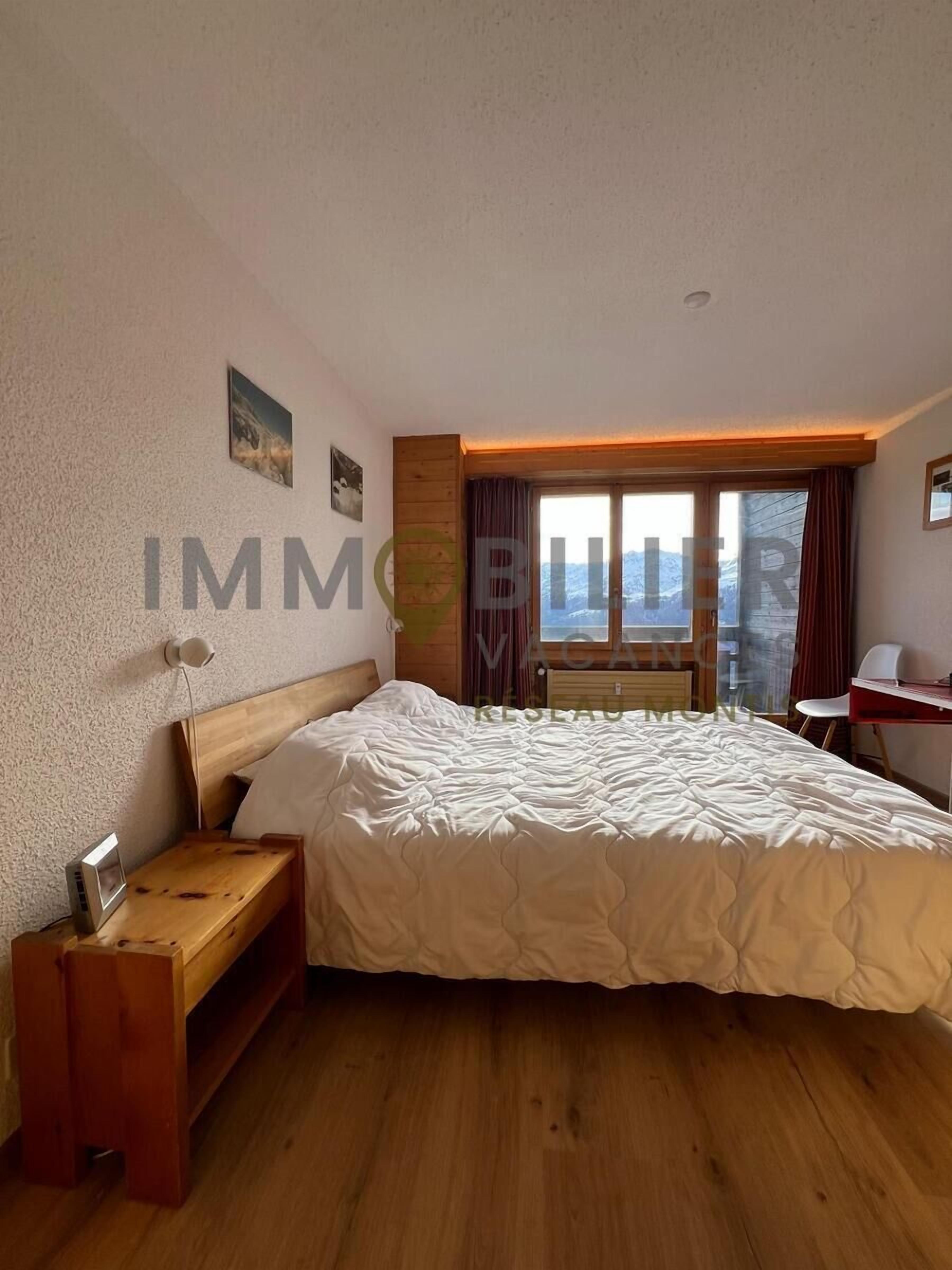 A bedroom with a wooden bed, a bedside table, a chair, and a window with curtains.
