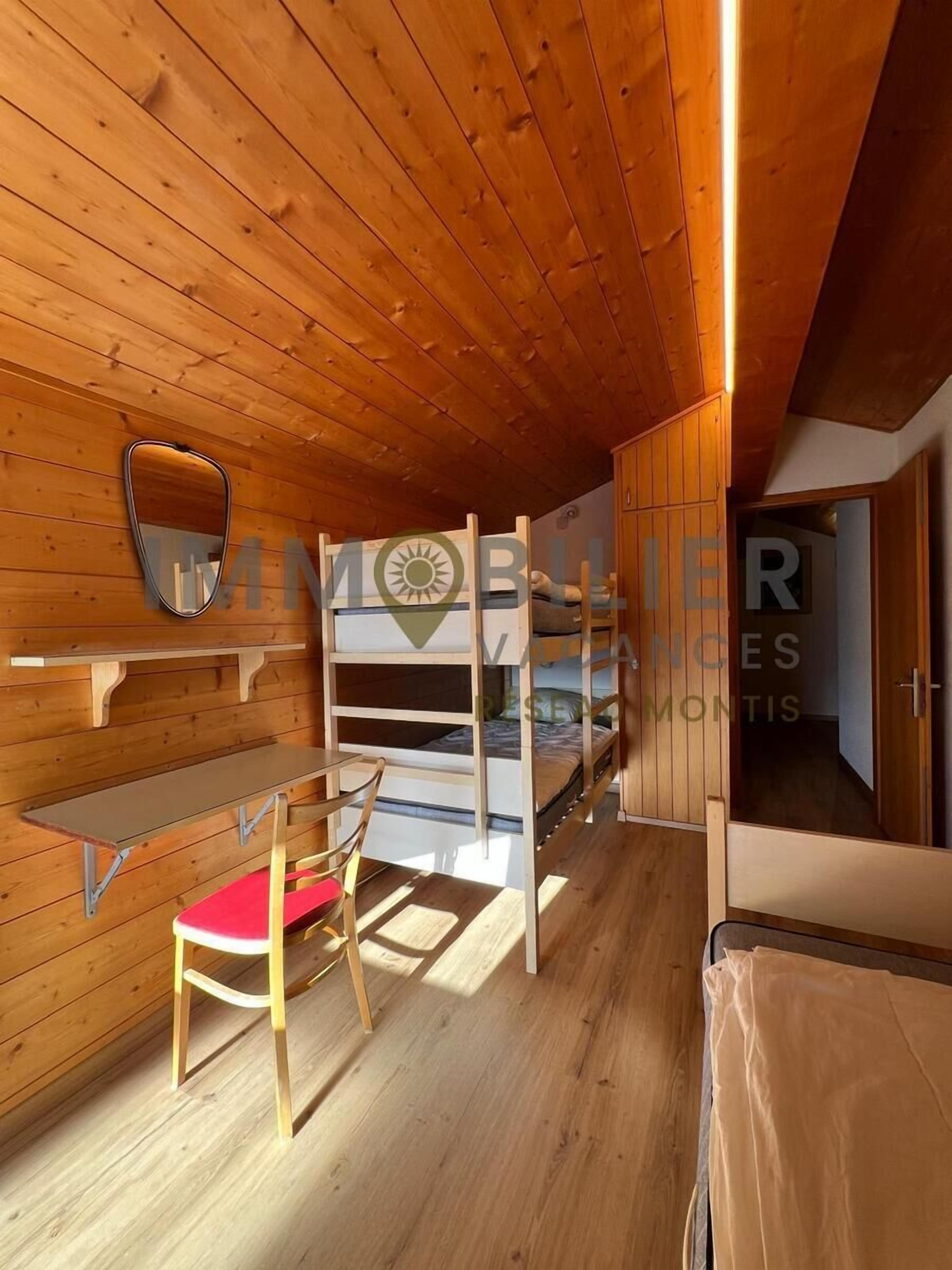 A compact room with a bunk bed, a small desk with a chair, and a mirror on the wall.