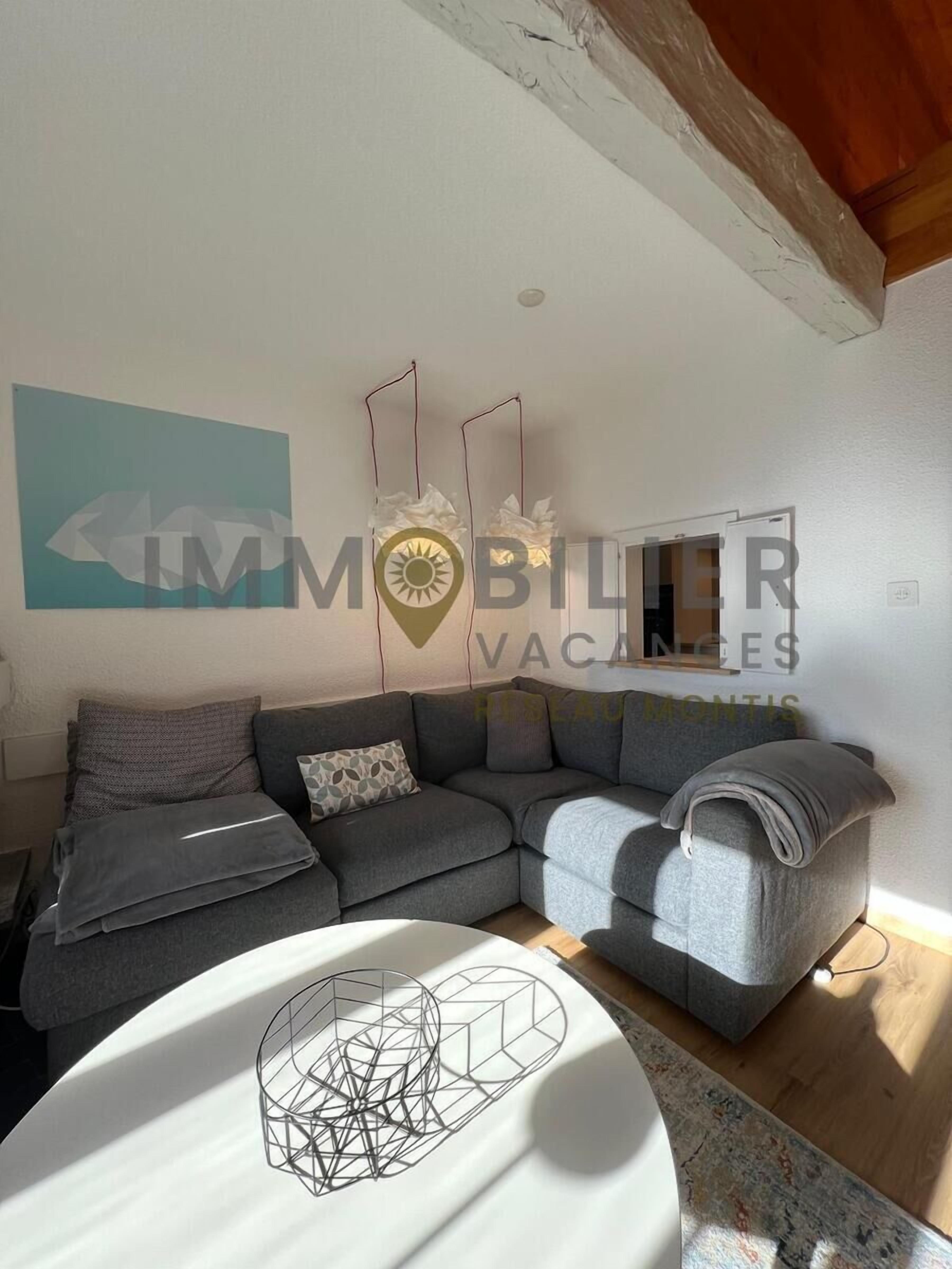 A modern living room with a grey sectional sofa, a white coffee table with a geometric metal sculpture, and a patterned rug.