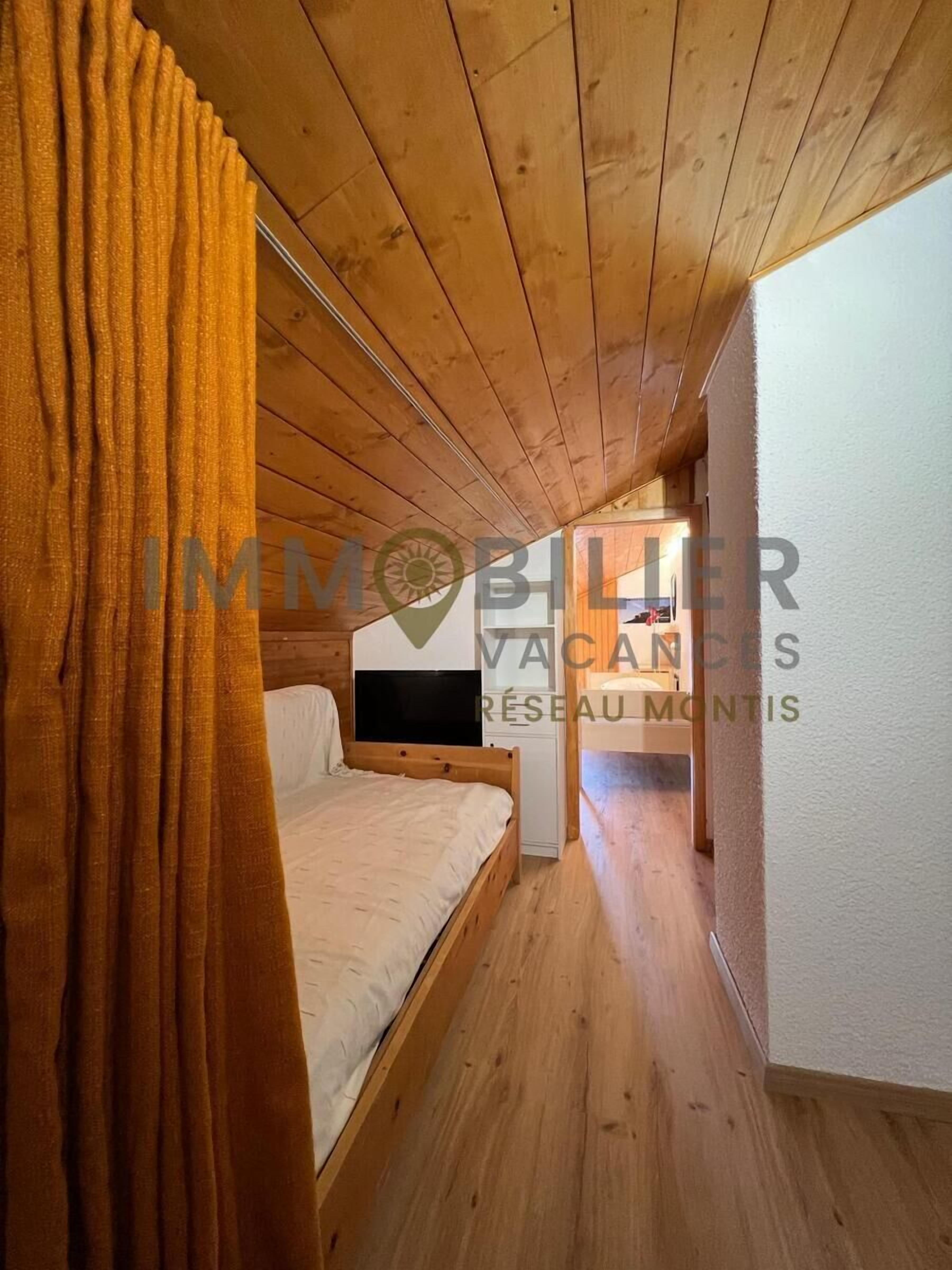 Une chambre avec un plafond en bois, un lit, une télévision et un rideau.