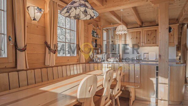 Un interior de madera con un largo banco y sillas, una zona de cocina y una mesa de comedor.