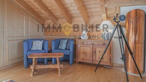 Interior de una cabaña de madera con dos sofás azules, una mesa de madera, un trípode y un barril de cobre.