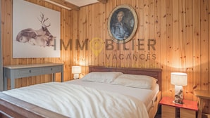 A wooden-paneled room with a bed, a nightstand, a lamp, and a framed portrait on the wall.