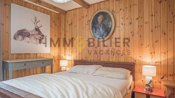 Une pièce aux murs lambrissés, contenant un lit, une table de chevet, une lampe et un portrait encadré accroché au mur.