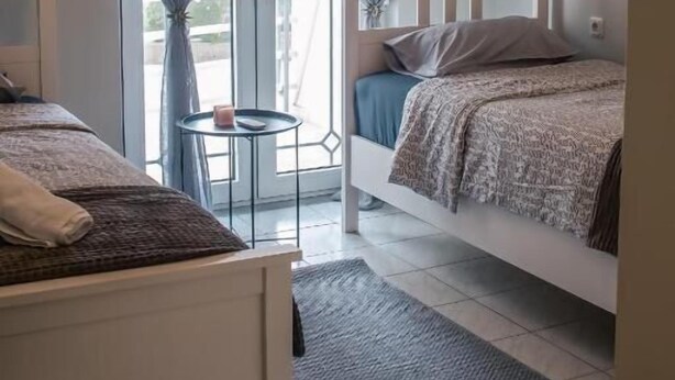 Un dormitorio con dos camas, una mesita redonda pequeña y un ventanal grande con cortinas.