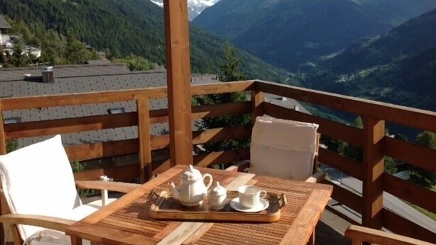 Una terraza de madera con una mesa lista para el té, con vistas a un paisaje montañoso.