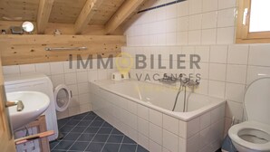 Un baño con techo de madera, azulejos blancos, una bañera, un inodoro y una lavadora.