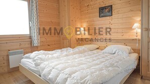 Un dormitorio con paneles de madera, una cama, una ventana con cortinas, un cuadro colgado en la pared y una lámpara de noche.
