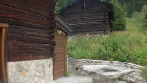 Une cabane rustique en rondins de bois, avec des fondations en pierre et un banc en pierre devant.