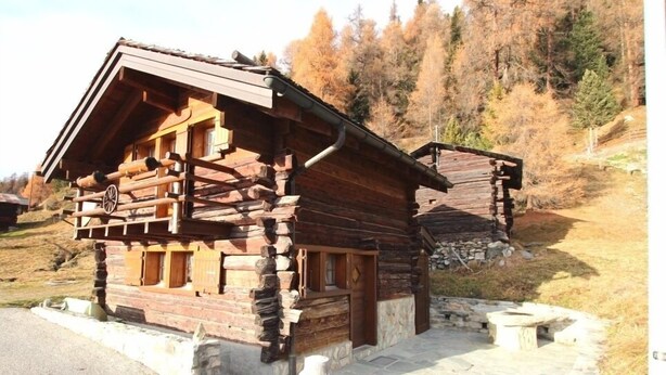 Une cabane rustique en rondins de bois, avec des fondations en pierre, une véranda en bois et une petite fenêtre.