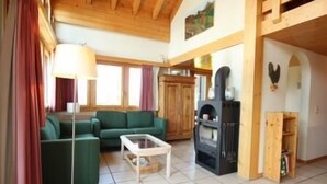A cozy living room with a green sofa, a white coffee table, and a wood-burning stove. - Très beau duplex combles plein sud, vue splendide ! Aisément accessible, à l'entrée du village, à pr (St-Luc)