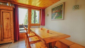 A wooden dining table with benches, a window with curtains, and a painting on the wall. - Très beau duplex combles plein sud, vue splendide ! Aisément accessible, à l'entrée du village, à pr (St-Luc)
