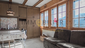 A cozy room with wooden walls, a dining table with chairs, a patterned sofa, and large windows with a view of mountains. - Spacious 2.5-room apartment with TV and Wi-Fi, south-west facing, with 2 large balconies, ideal for (St-Luc)