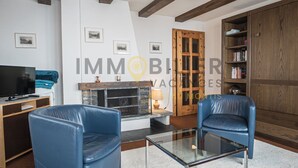 A living room with a fireplace, two blue leather chairs, a glass coffee table, a TV, and a bookshelf. - Spacieux et lumineux 3.5 pièces pour 4 à 6 personnes, situé au 1er étage (angle ouest) d'une résiden (St-Luc)