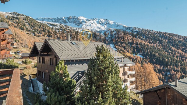 A mountain lodge with a wooden exterior, a ski lift in the background, and a clear view of snow-capped mountains.