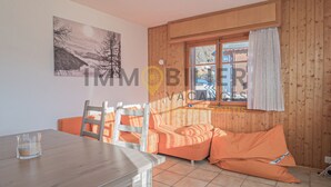 A room with a wooden interior, a dining table, orange seating, a window with curtains, and a painting on the wall.