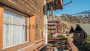 A wooden building with a balcony, a window with a curtain, and a view of a mountain.