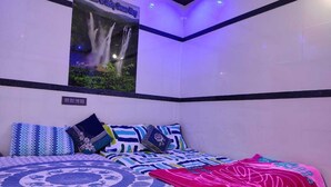 A bedroom with a bed, pillows, a poster, and a ceiling light fixture. - Ruby Home Stay (Sagara)